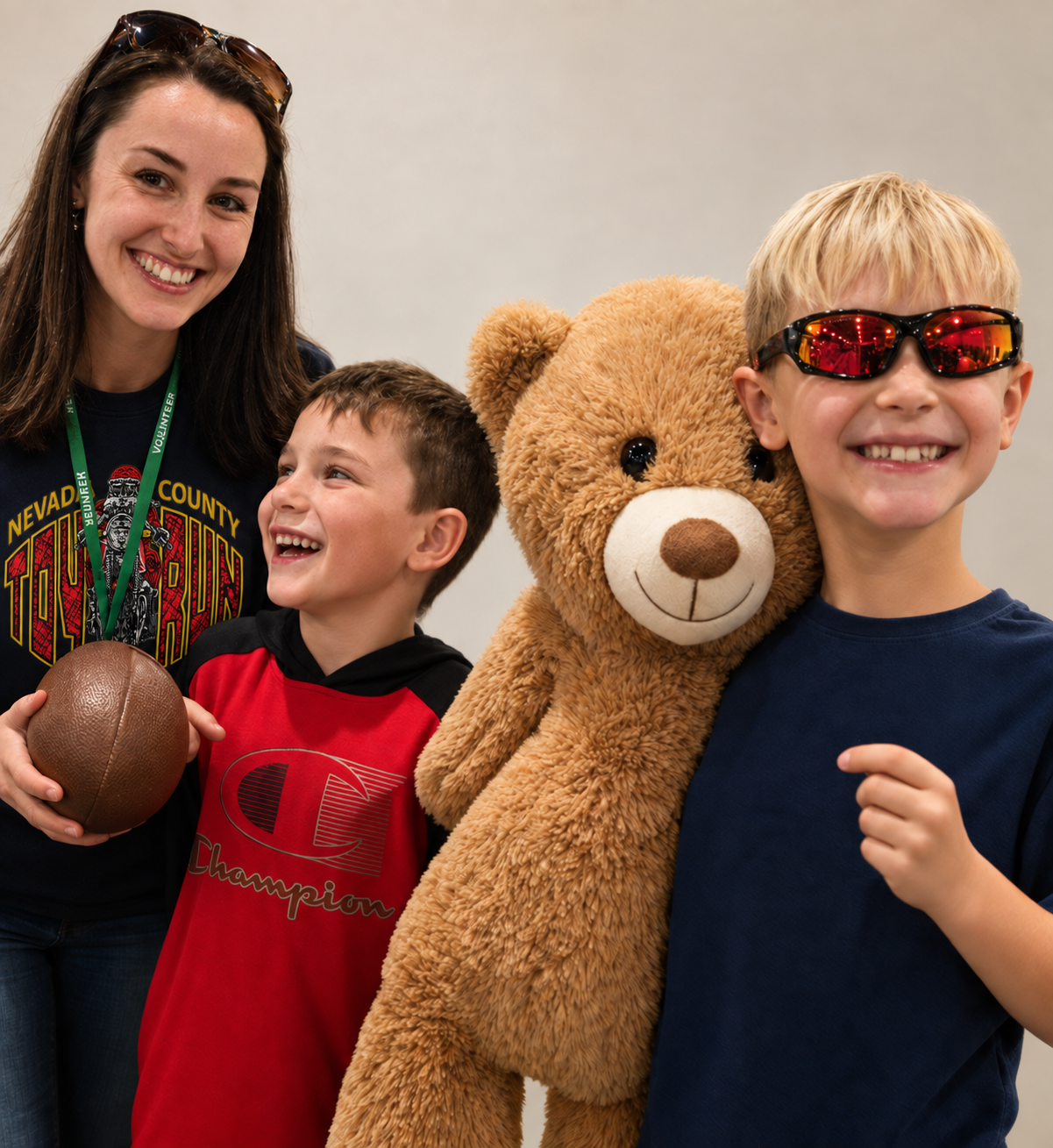 A Nevada County Toy Run volunteer with two smiling children and a large teddy bear.